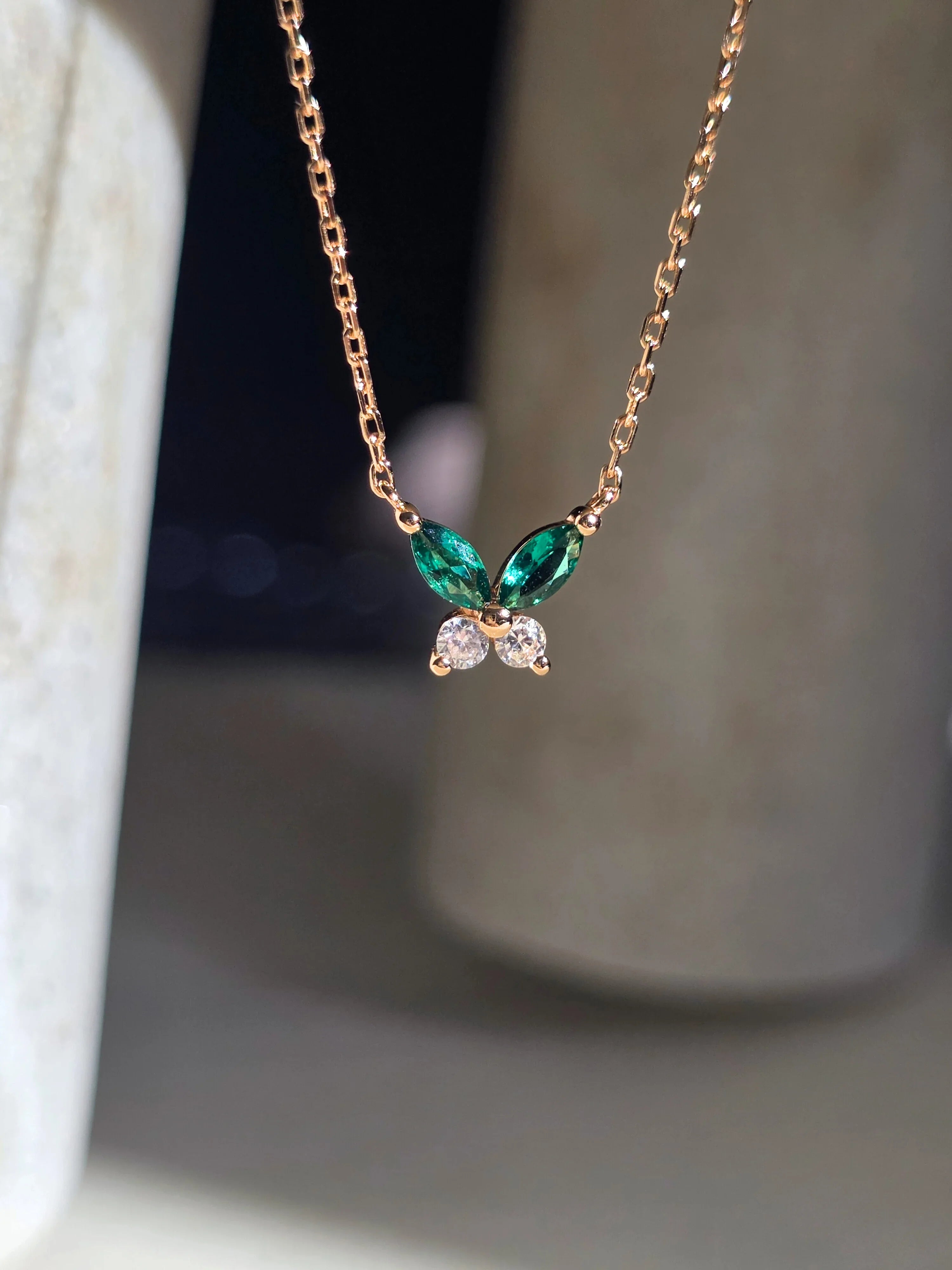 Gold necklace with green and clear gemstones on a neutral background- front