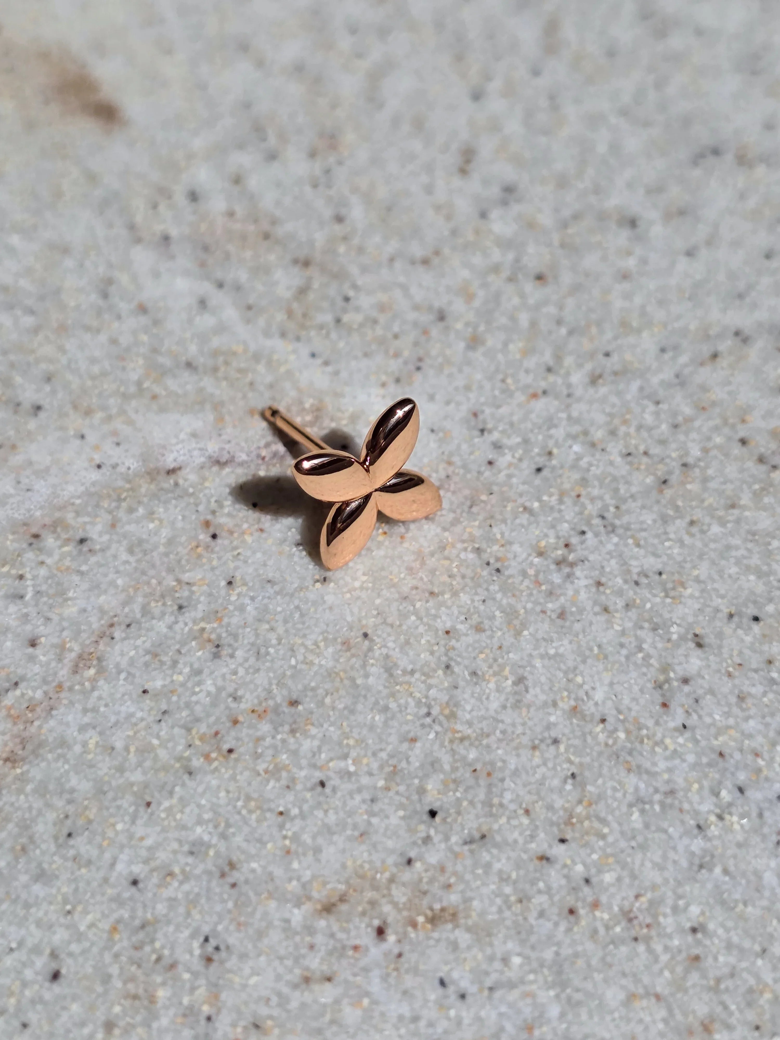Rose gold butterfly-shaped earring on a textured beige surface- front